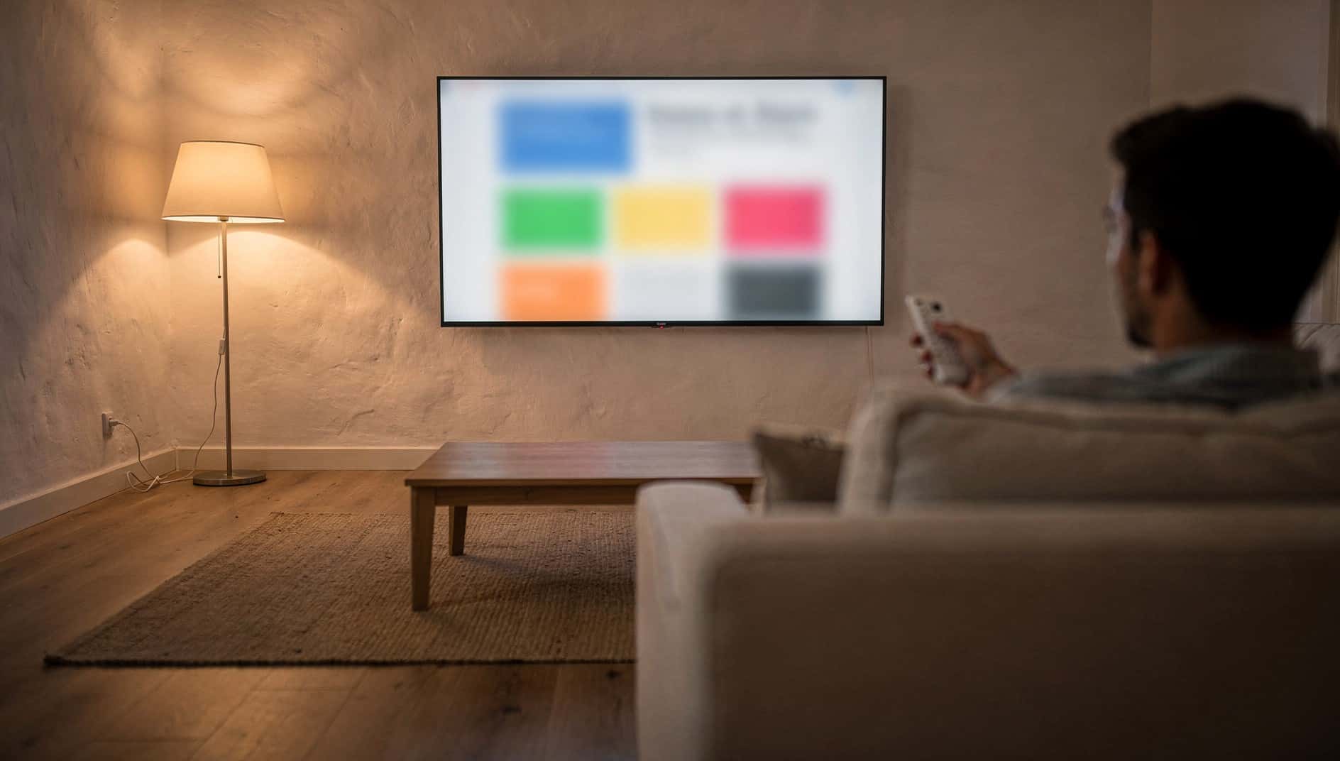 Hombre en el sofá con el mando apuntando a una televisión que muestra una web