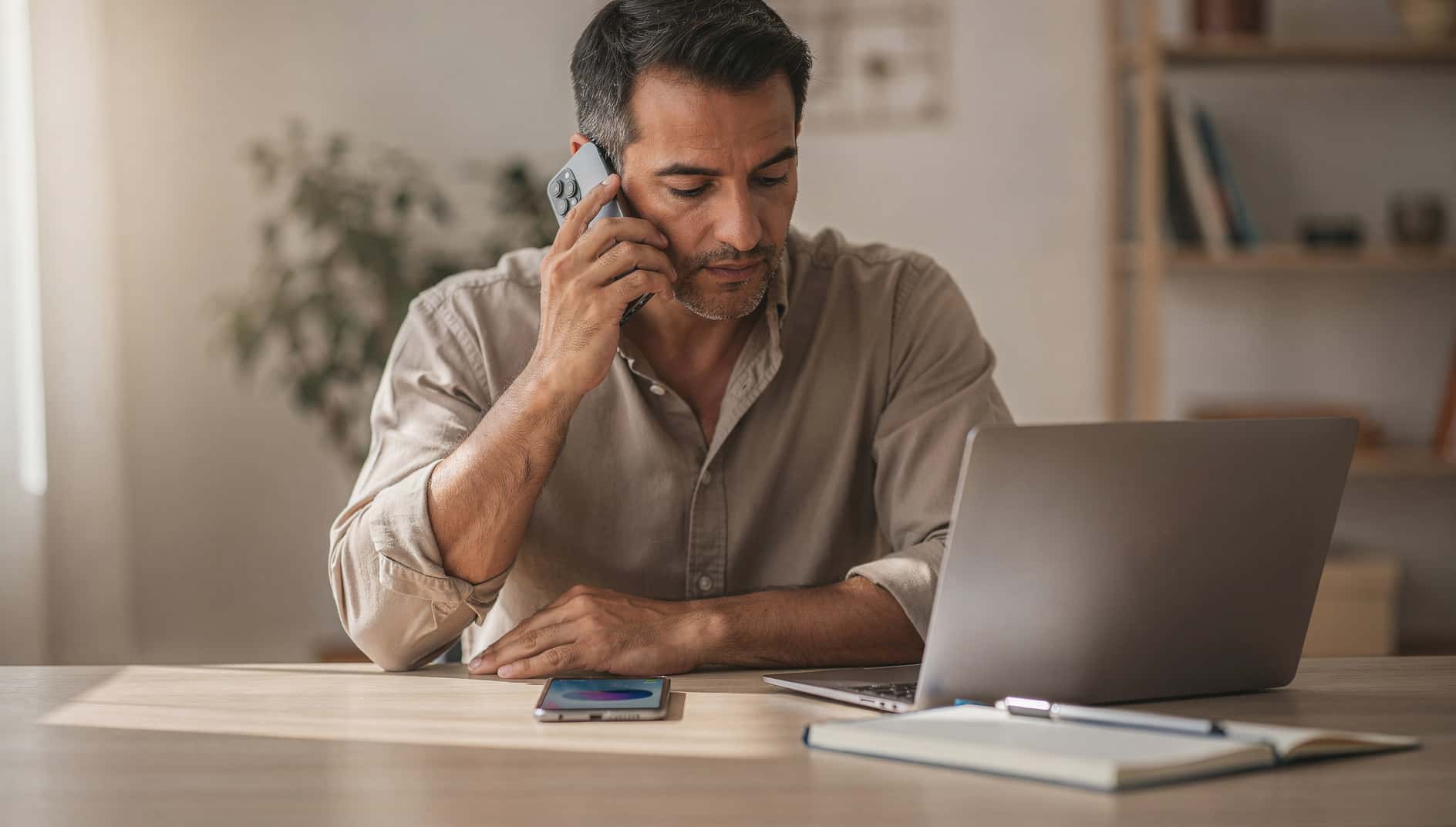 Hombre en su escritorio hablando por el móvil con otro teléfono sobre la mesa