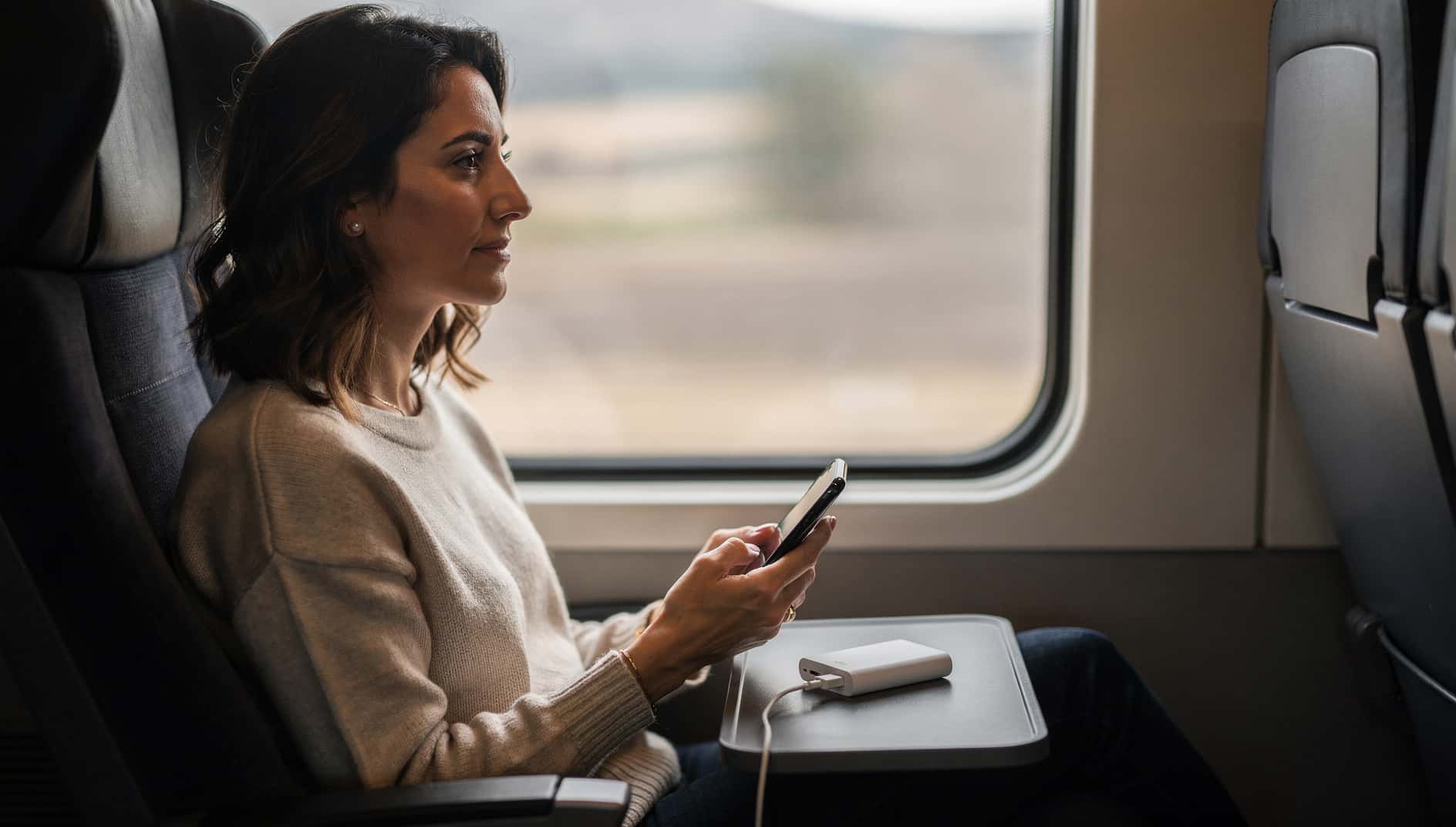 Mujer en un tren cargando el móvil con una batería externa