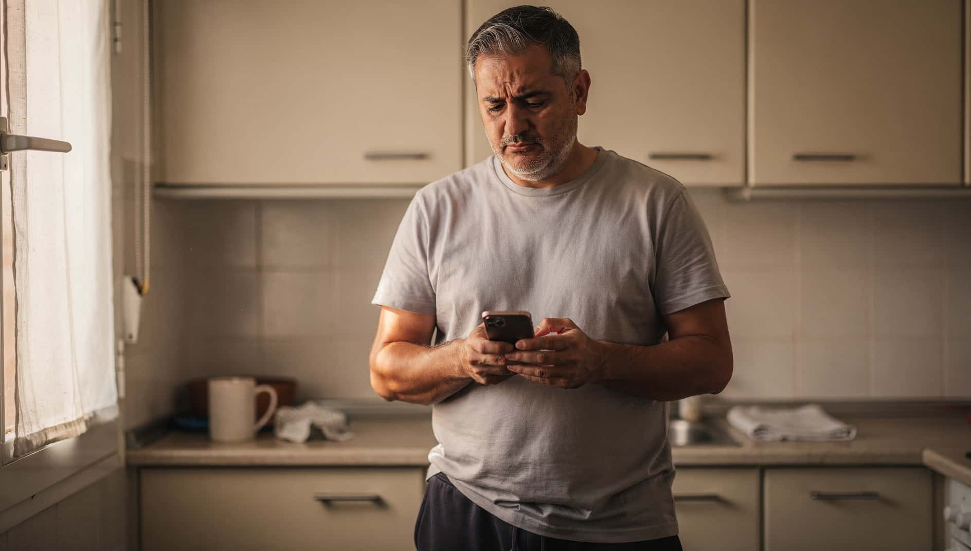 Hombre en la cocina apartando con fastidio el móvil que está sonando