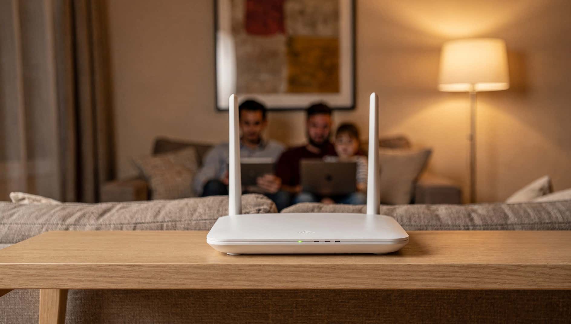 Router wifi sobre una mesa, con una familia usando portátil y tableta en el sofá