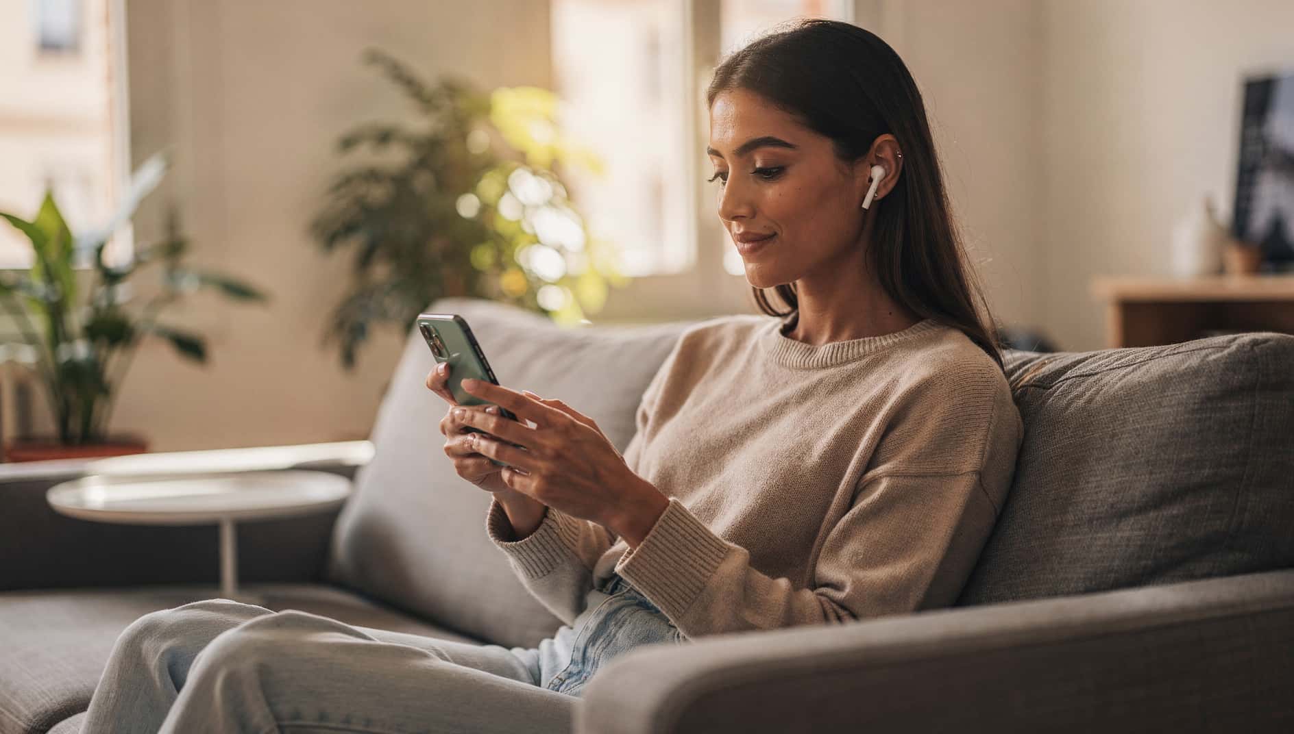 Mujer en un sofá usando su móvil Android con auriculares inalámbricos