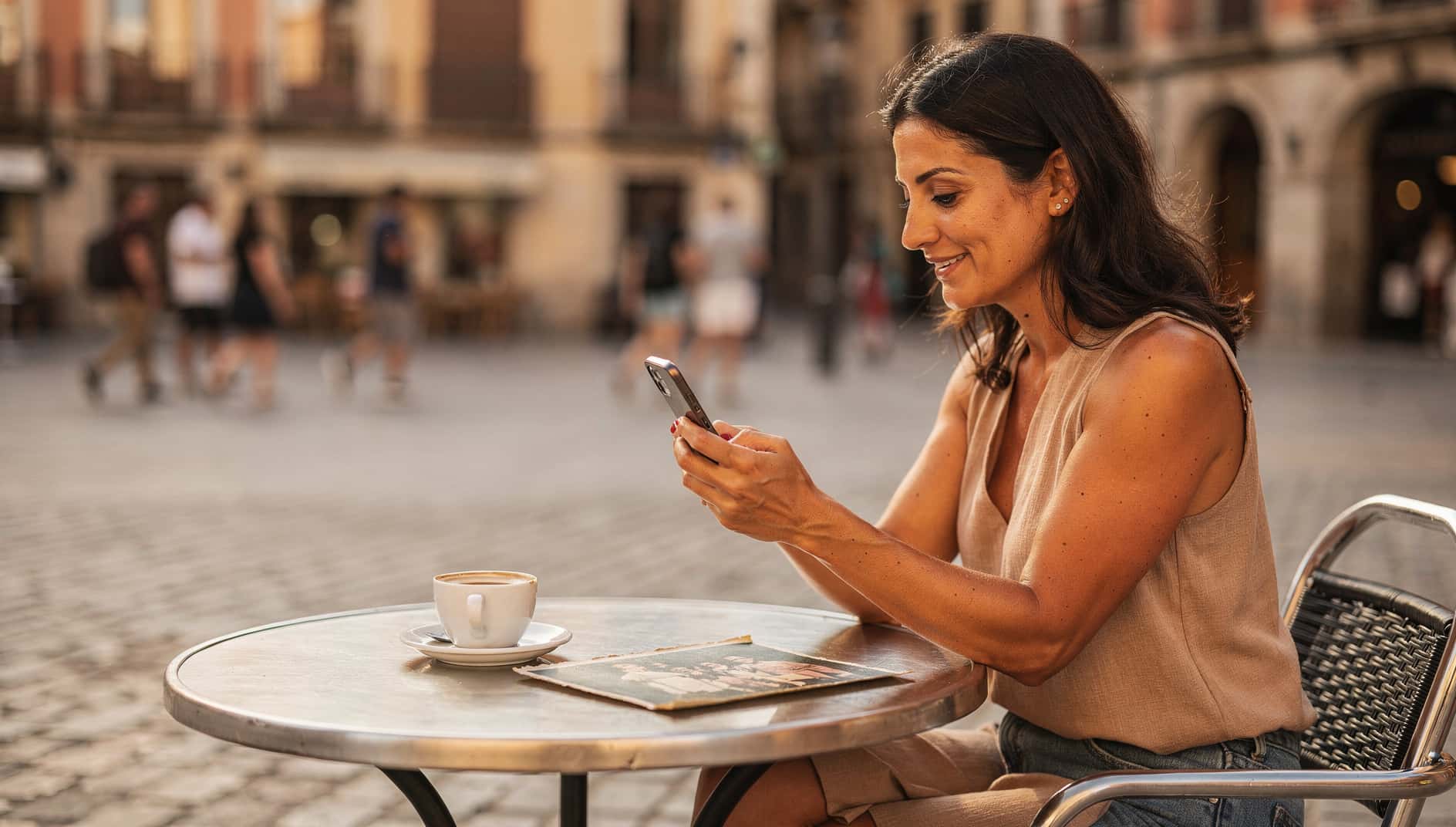 Mujer en una terraza mirando el móvil junto a una foto antigua impresa