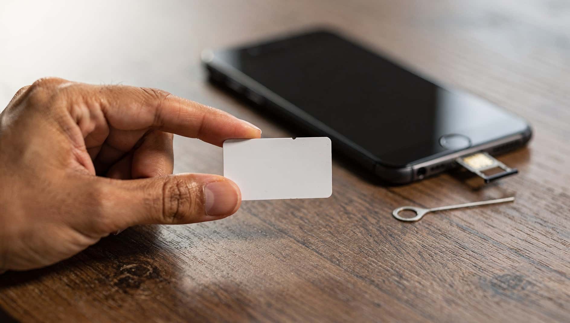 Mano que sostiene una tarjeta SIM junto a un móvil con la bandeja de la SIM abierta