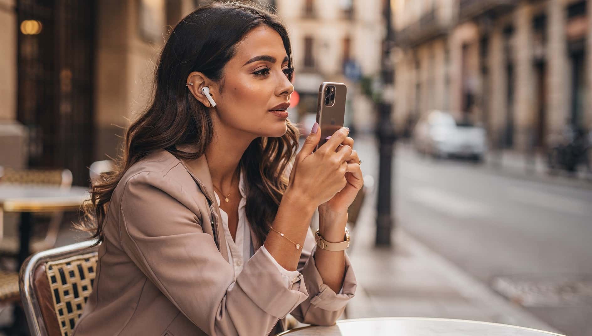 Mujer con auriculares inalámbricos grabando un mensaje de voz con el móvil en una terraza