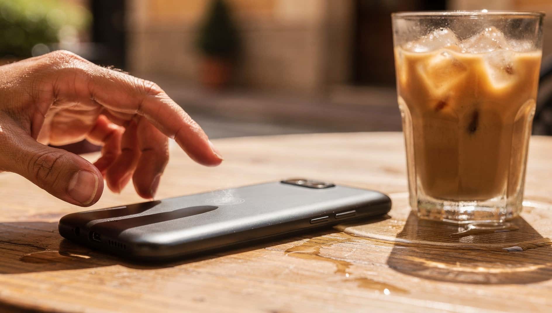 Móvil al sol sobre la mesa de una terraza junto a un café con hielo