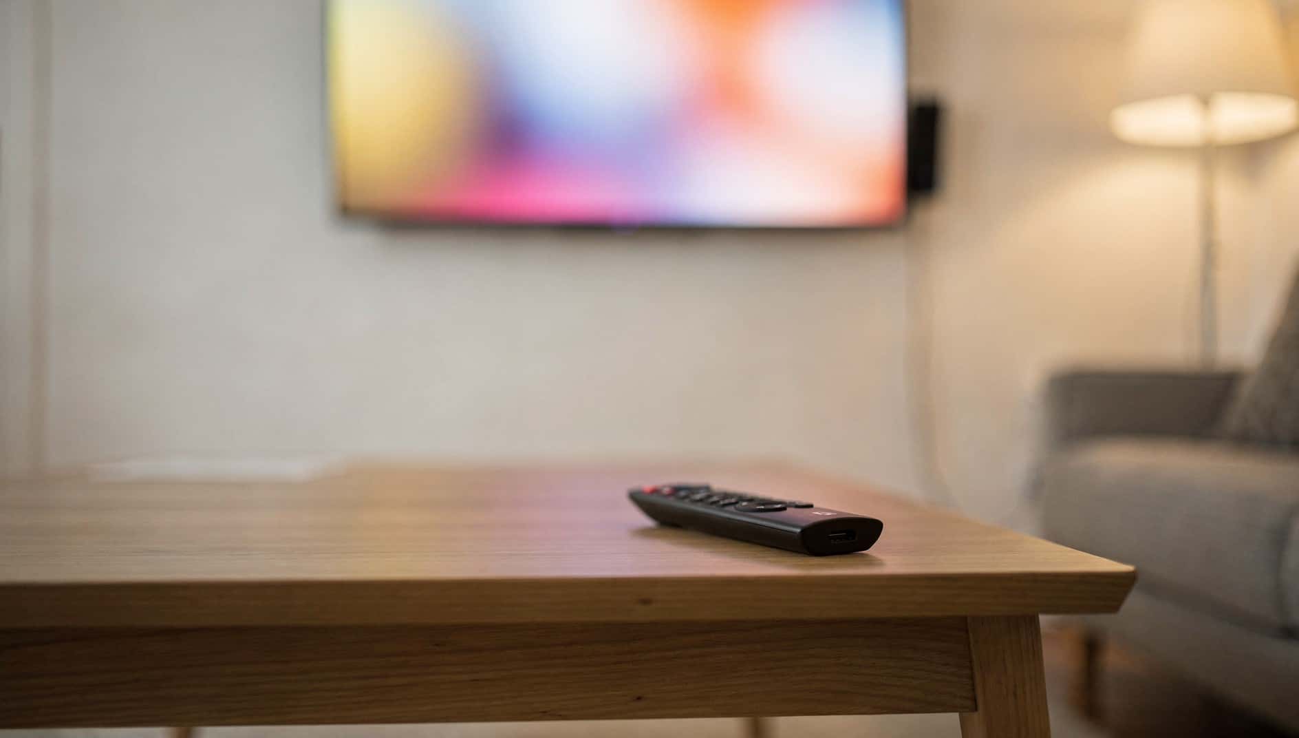 Salón con una televisión encendida en la pared y un mando a distancia sobre la mesa
